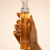 Prume parfumée Midnight Elixir GlowlyGlow pour le corps et les cheveux, tenue en main sur fond beige.